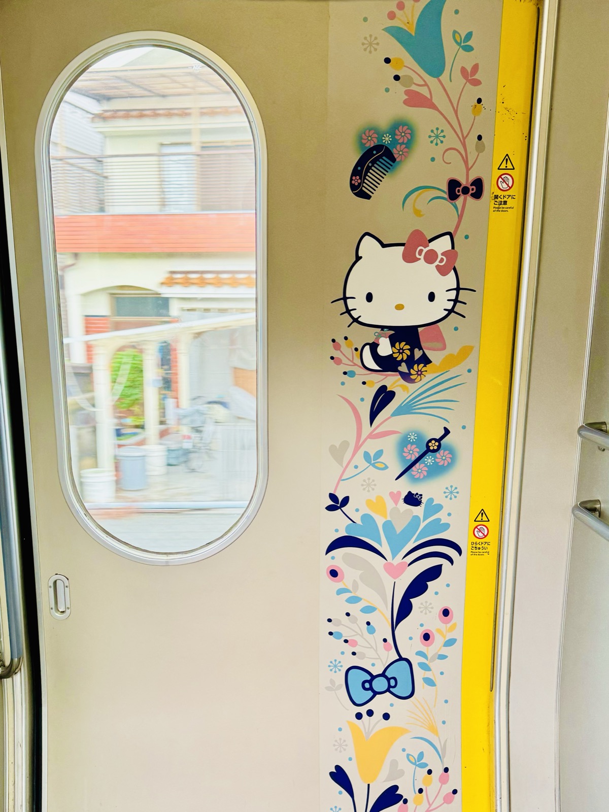 Interior of a train decorated with Hello Kitty illustrations, houses visible through the door window