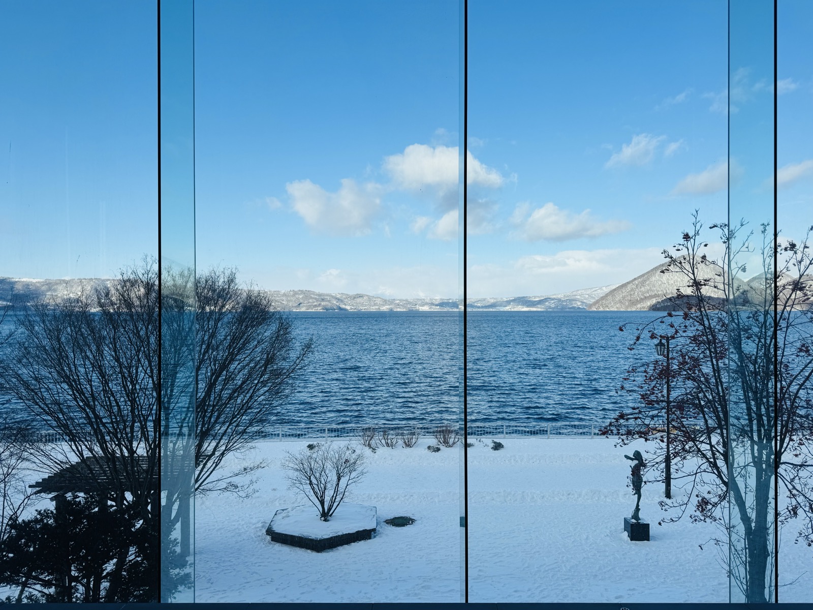 A snowy lakeshore and distant mountains seen through tall windows at Lake Tōya
