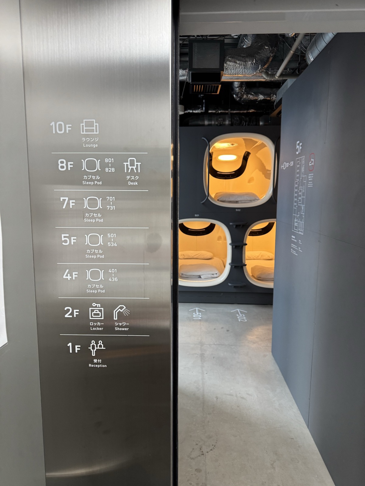 A capsule hotel floor directory beside glowing sleep pods