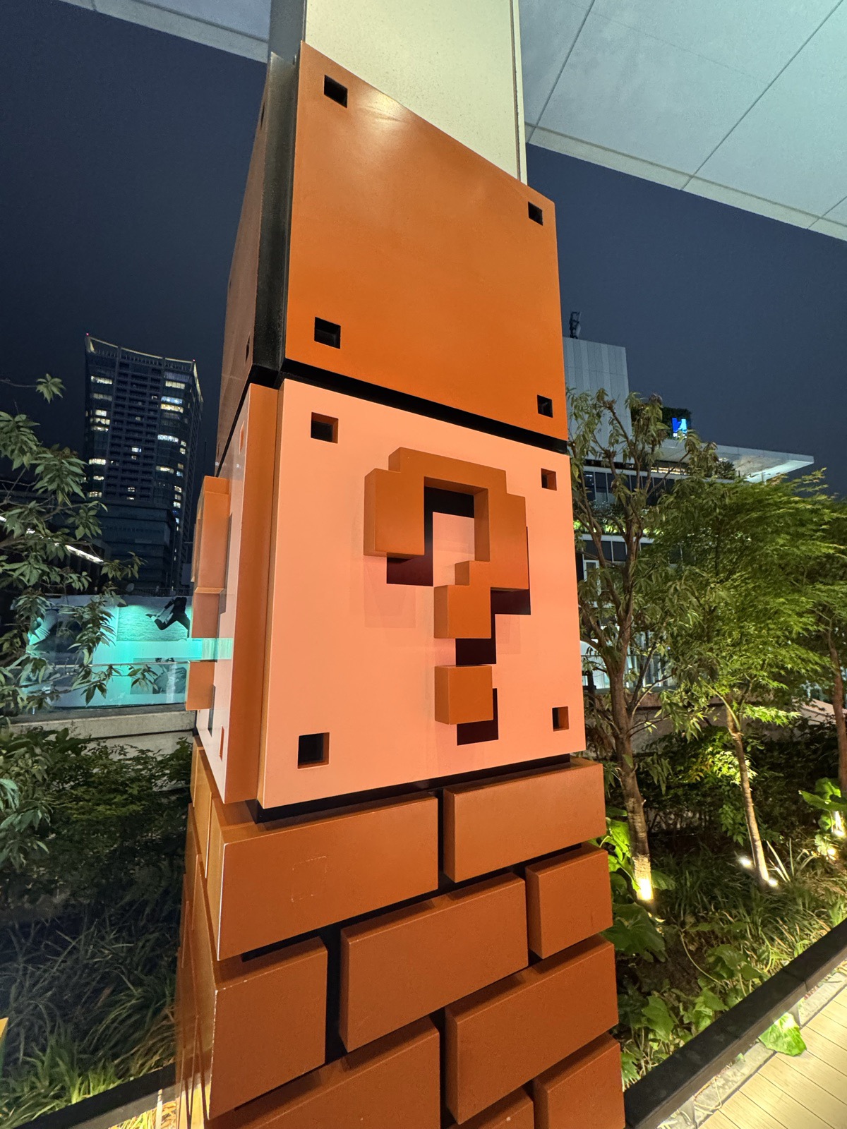 A large Super Mario question-mark block sculpture on brick, lit at night