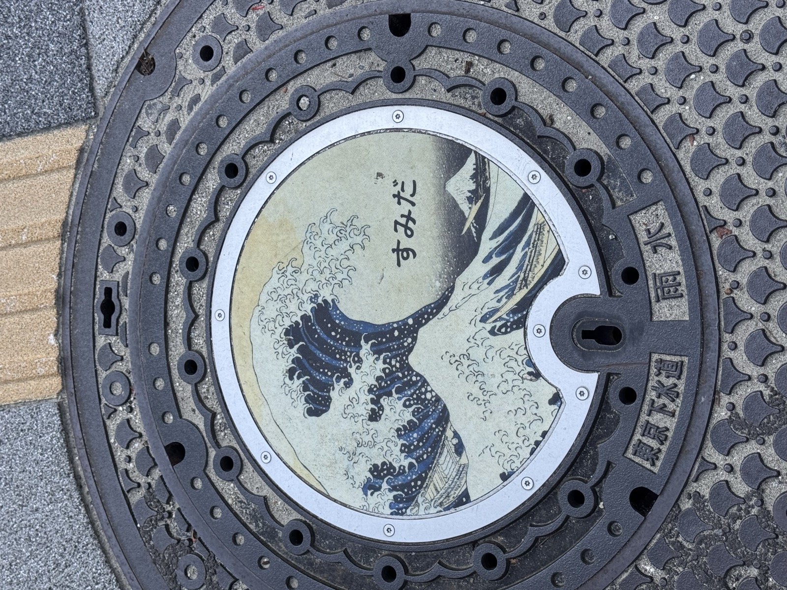 A manhole cover painted with Hokusai's Great Wave and the word Sumida
