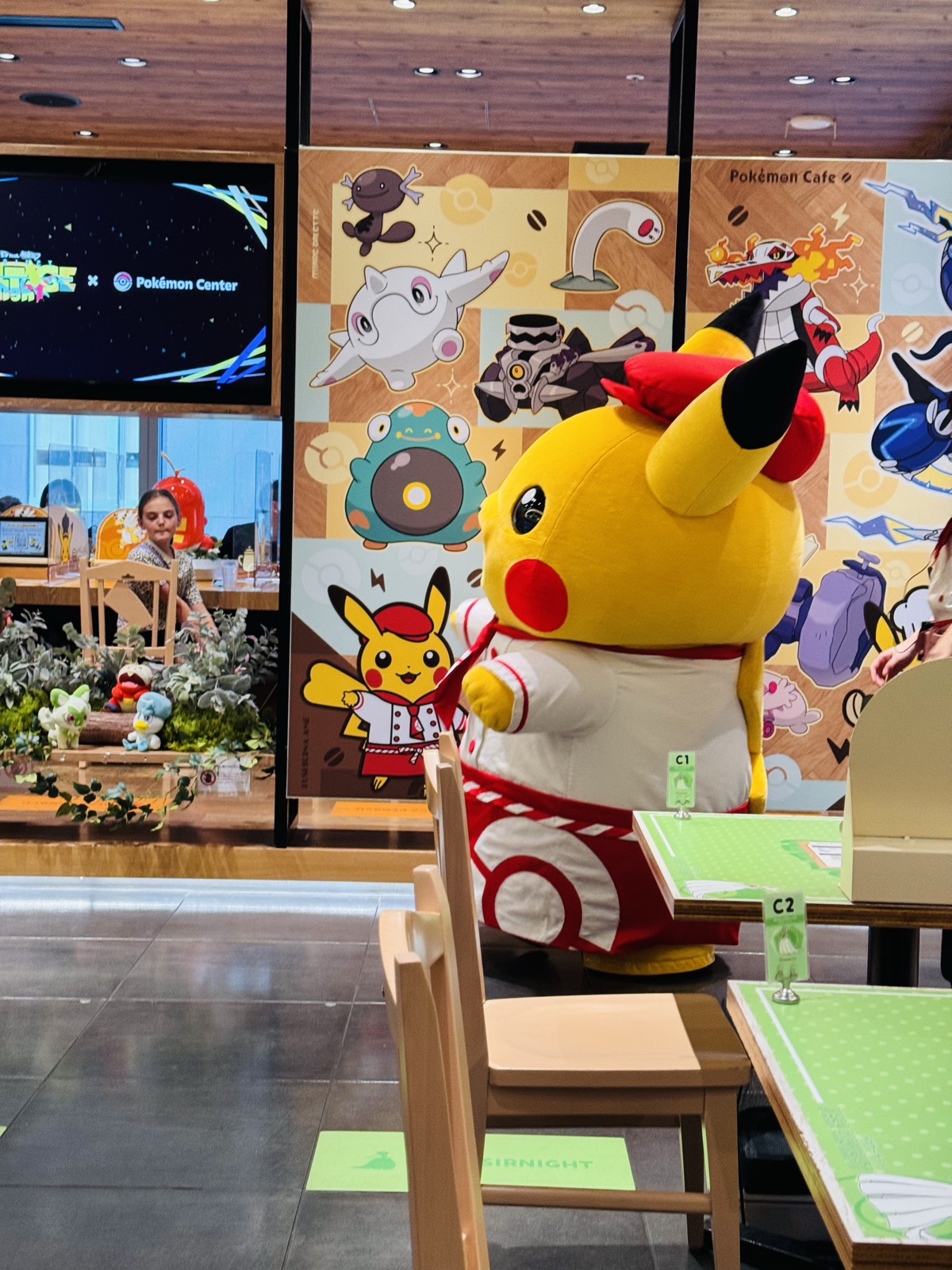 A giant chef Pikachu mascot greeting tables inside the Pokémon Café