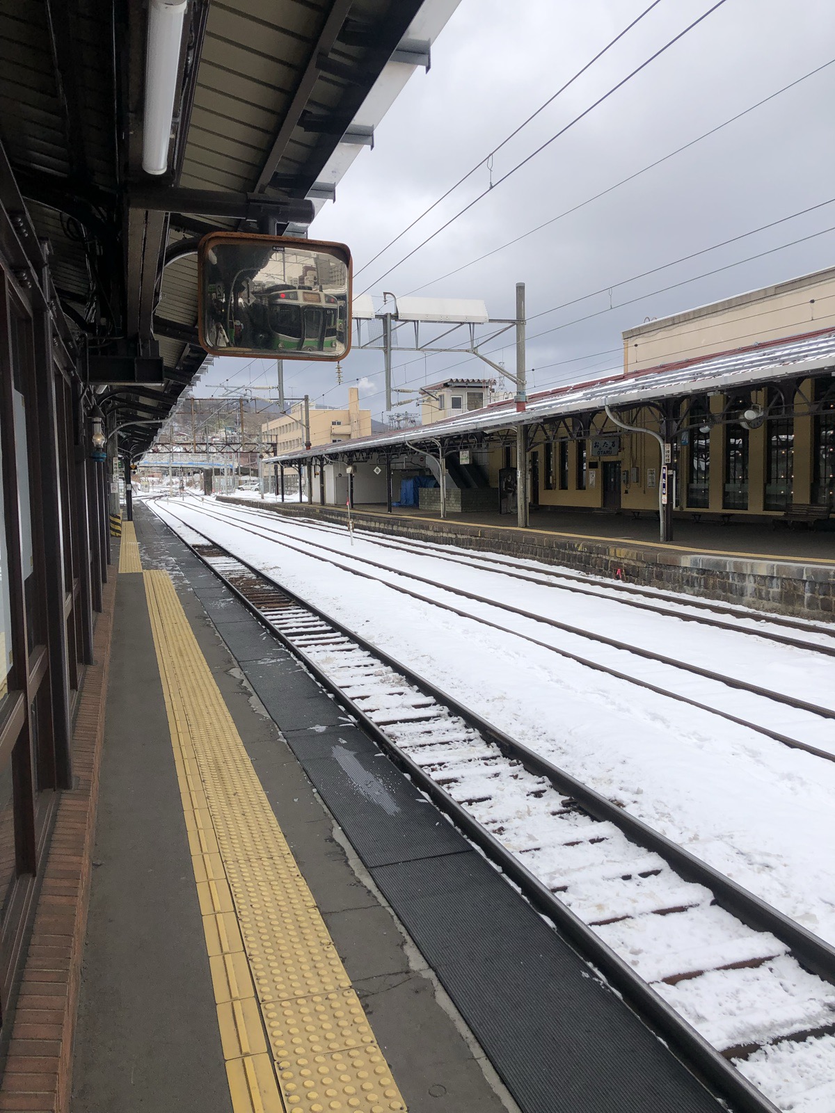 A quiet snow-covered railway platform with tracks and a convex mirror